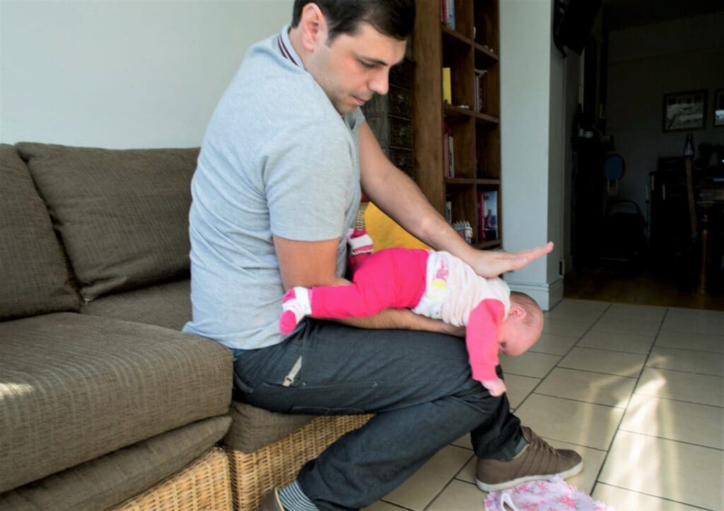 Step one - five back blows
Hold the baby face-down along your thigh with their head lower than their bottom.
Hit them firmly on their back between the shoulder blade up to five times. If back blows do not dislodge the blockage, move onto step 2.